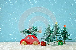 Red wooden car carrying a christmas tree over snow in front of blue background.