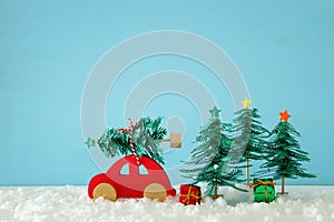 Red wooden car carrying a christmas tree over snow in front of blue background.
