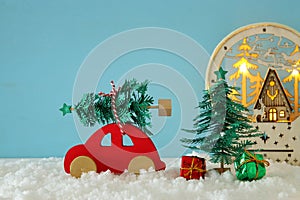Red wooden car carrying a christmas tree over snow in front of blue background.