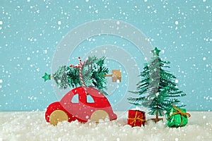 Red wooden car carrying a christmas tree over snow in front of blue background.