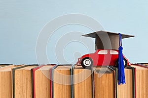 Red wooden car toy with graduate cap on textbook blue wall background copy space - Back to school, education and scholarship