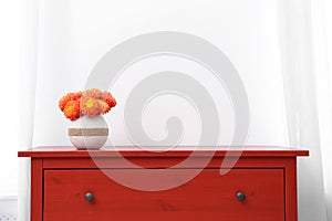 Red wooden chest of drawers with fresh flowers near wall indoors