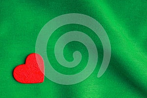 Red wooden decorative heart on green folds background.