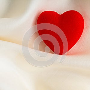 Red wooden decorative heart on white silk background.