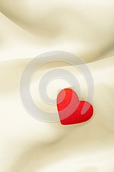 Red wooden decorative heart on white silk background.