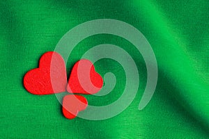 Red wooden decorative hearts on green folds background.