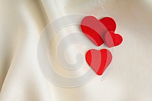 Red wooden decorative hearts on white silk background.