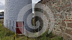 The red wooden door at the base of the Montrose Port Rear Lighthouse, with its whitewashed stone curved wall.