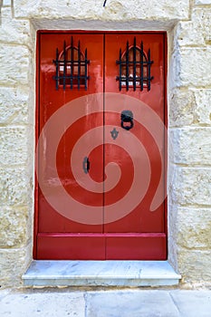 Red wooden door with black forged vintage lion head shaped ring knocker and gratings on small windows