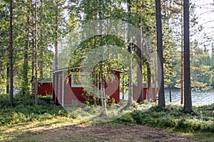 Red wooden finnish cabins cottages in green pine forest near river. Rural architecture of northern Europe