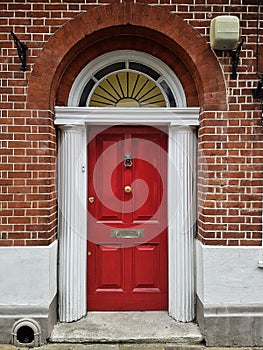 Red wooden front door with arch and pillars at a brick building.