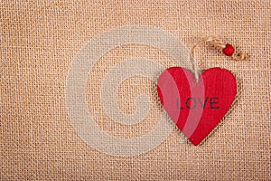 Red wooden heart pendant on a natural linen background. A wooden valentine on a natural background. Backgrounds and textures.