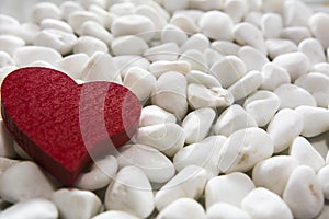 Red wooden heart on a white pebble background.