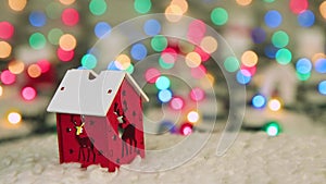 Red wooden house with deer on the background of Christmas lights.