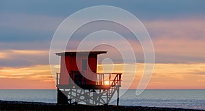 Red wooden lifeguard rescue tower on the empty beach with sunset cloudy sky background