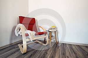 Red wooden modern armchair with opened book and yellow flowers on the small table near it.