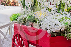 Red wooden wheelbarrow with wooden boxes full of blooming artificial flowers. Street and garden decoration