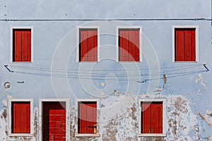 Red wooden windows and door on old light blue wall, on the island of Burano, in Venice, Italy