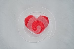 Red wool felted heart lying on white sheet