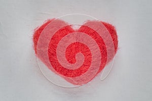 Red wool felted heart lying on white sheet close up