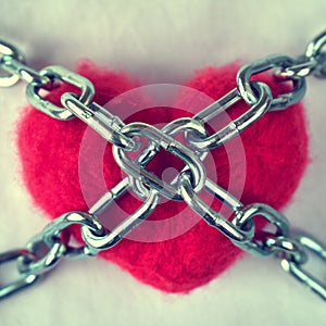 Red wool heart locked with metal chain on white bed sheet