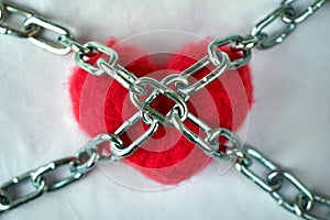 Red wool heart locked with metal chain on white bed sheet