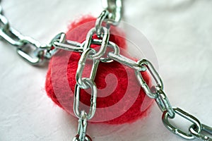 Red wool heart locked with metal chain on white bed sheet