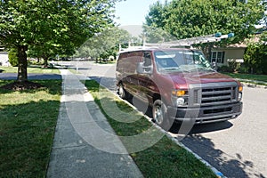Red workman's van with ladders on top parked on a tree lined street