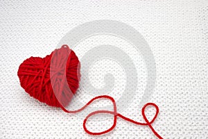 Red yarn ball like a heart on the white crochet background. Romantic Valentines Day concept. Red heart made of wool yarn with plac