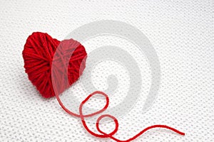 Red yarn ball like a heart on the white crochet background. Romantic Valentines Day concept. Red heart made of wool yarn with plac