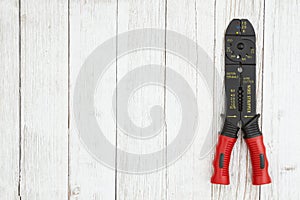 Red, yellow and black wire stripper tool weathered whitewash textured wood background