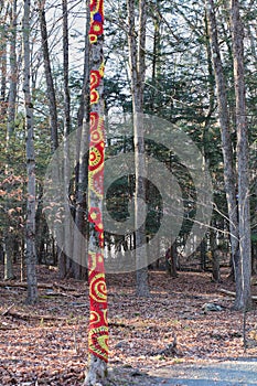 Red and yellow crochet trees in woods on a trail.
