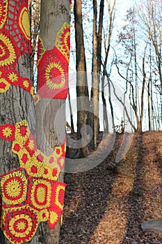 Red and yellow crocheted trees in woods on a trail path..