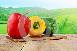 Red yellow green bell peppers on wooden and nature background.