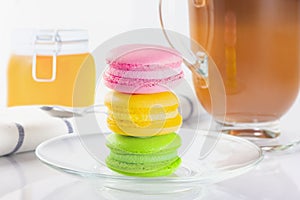 Red, yellow and green macaron cupcakes in a glass plate. Coffee in an Irish coffee glass, orange jam in a jar with a yoke. Linen n