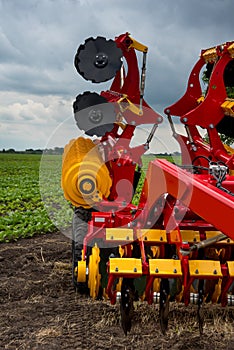 red and yellow harrow-cultivator standing folded for transportation near a field