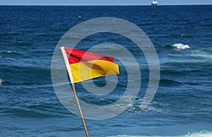 RED AND YELLOW LIFEGUARD FLAG WITH SEA IN BACKGROUND