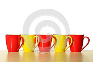 Red and yellow mugs in a row on wooden table. White background