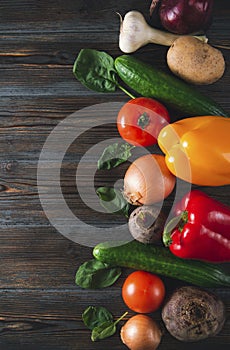 Red and yellow peppers, green cucumbers, garlic, beetroot, tomato, spinach, potatoes,  onions,   on a brown wooden   top view,