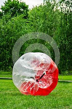 Red Zorbing Balloon on the summer lawn. Inflatable zorb ball outdoor. Leisure activity concept with vertical copy space