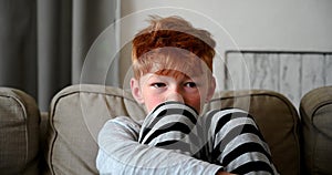 Reddish boy with red hair sitting on sofa sad watching tv alone