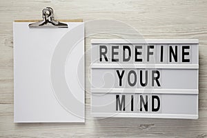 `Redefine your mind` words on modern board, noticepad over white wooden background, top view. Overhead, flat lay