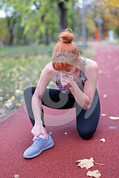 Redhaed woman in sportswear with painful ankle injury on running track