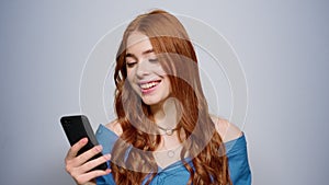 Redhair girl holding mobile phone in studio. Woman getting good news indoors