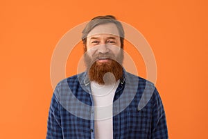 Redhaired bearded man stands smiling to camera against orange background
