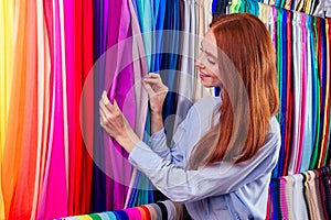 Redhaired ginger business woman working at textile shop.Redhead salewoman in storage update cotton and lace fabric