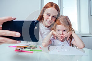 Redhaired ginger sisters painting together at house in the morning and kaking selfie photo on camera of smartphone