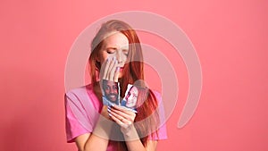 Redhaired ginger woman in pink studio background tearing photo card of smiling international couple