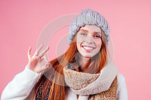 Redhaired ginger woman wear stylish wool hat ,sweater and scarf looking at camera and pointing fingers okay at copyspase