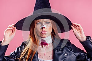 Redhaired ginger woman witch black hat and in leather jacket take thought and scaring with crazy make up on her pretty